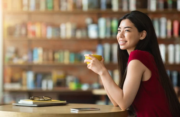 Pausa para el café. Pensativo chica asiática disfrutando de taza de bebida caliente en café — Foto de Stock