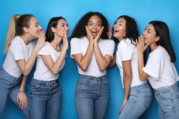 Jeunes femmes chuchotant secret à un ami sur fond bleu — Photo