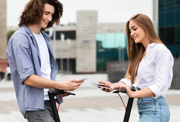 Friends riding on motorized kick scooters, holding phones — Stock Photo, Image