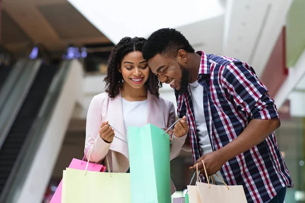 Happy black couple discussing purchases in shopping center, opening bags and smiling — Stock Photo, Image