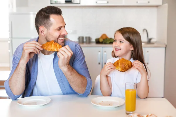 Baba ve kızı kahvaltıda kruvasan yiyor. Mutfakta oturuyor. — Stok fotoğraf