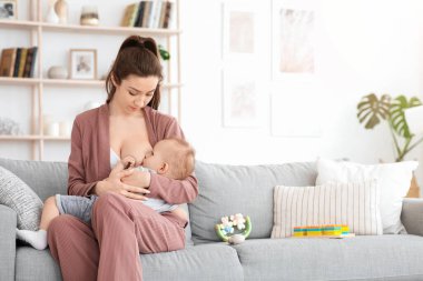 Emzirme Konsepti. Evdeki kanepede bebeğini emziren genç bir kadın.