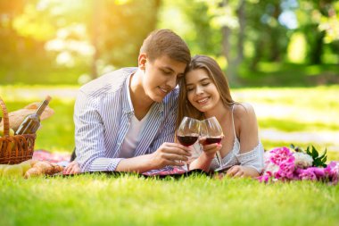 Sevecen genç çift piknik battaniyesinde yatıyorlar, dışarıda kırmızı şarap bardaklarıyla.