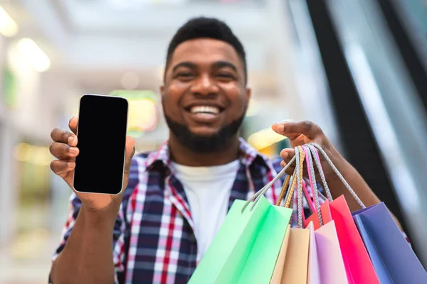 App de compras. Sorrindo homem demonstrando smartphone com tela preta no shopping — Fotografia de Stock