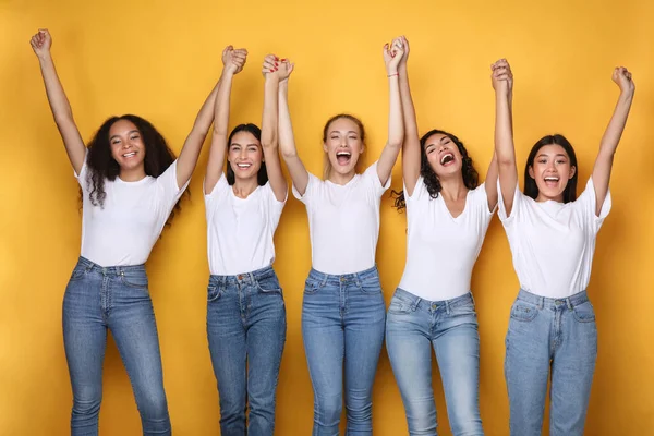 United Diverse Girls Holding Raised Hands Smiling Over Yellow Background — Stock Photo, Image