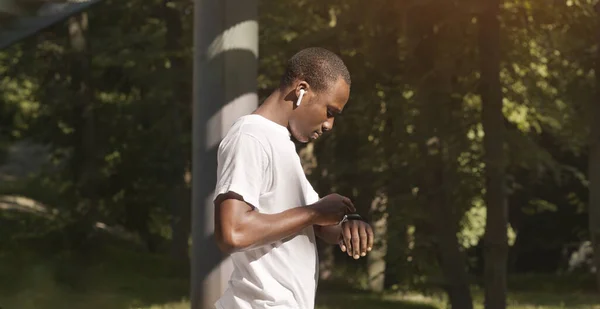 Africano americano em fones de ouvido verificando sua atividade em smartwatch — Fotografia de Stock