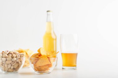 Fıstık, cips ve nachos tabakta. Bir bardak bitmemiş light bira ve bir şişe bira.