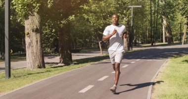 Kulaklıklı siyah bir adam parkta koşuyor, boş bir alan.