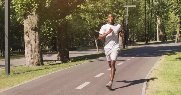 Kulaklıklı siyah bir adam parkta koşuyor, boş bir alan. — Stok fotoğraf