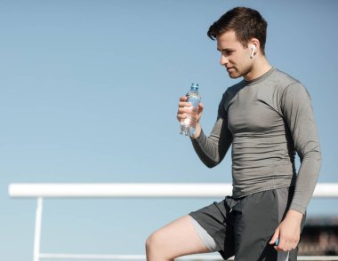 Spor için su. Spor giyim sektöründe yorgun adam elinde şişeyle koşuyor.