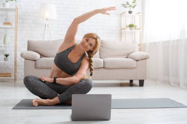 Evde pilates, yoga ve fitness yapıyorum. Kadın esneme egzersizleri yapıyor, nilüfer çiçeğinin üstünde oturuyor.