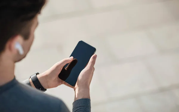 Favorite music for workout. Guy in modern wireless headphones and with tracker uses smartphone — Stock Photo, Image