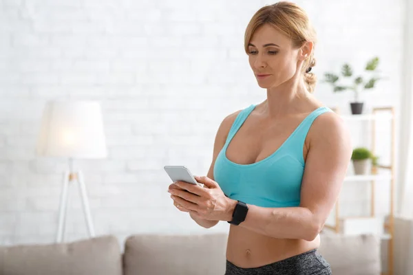 Treino de força e cardio aeróbico. Treinador mulher com smartwatch olha para o telefone — Fotografia de Stock