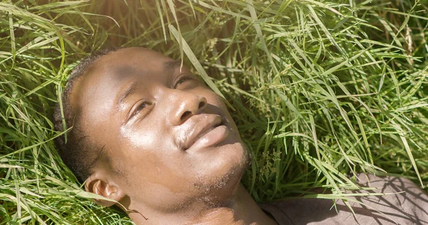 Friedlicher afrikanisch-amerikanischer Typ entspannt sich in der Sonne, liegend im Gras — Stockfoto