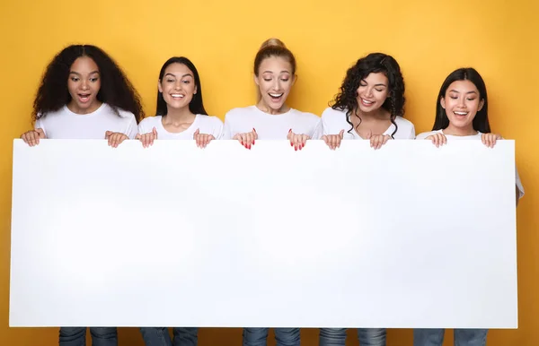 Chicas emocionadas sosteniendo cartel vacío para texto, fondo amarillo, burla — Foto de Stock