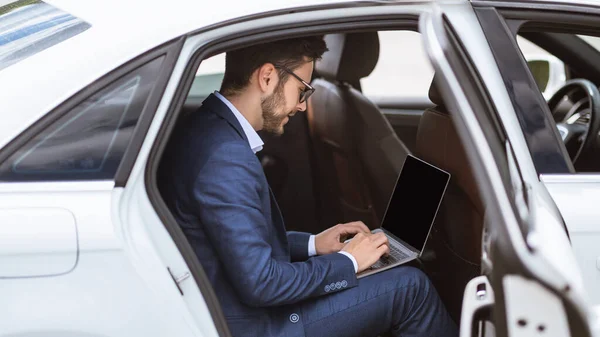 Ung affärsman använder bärbar dator med tom skärm på baksätet i sin bil, mockup för design — Stockfoto