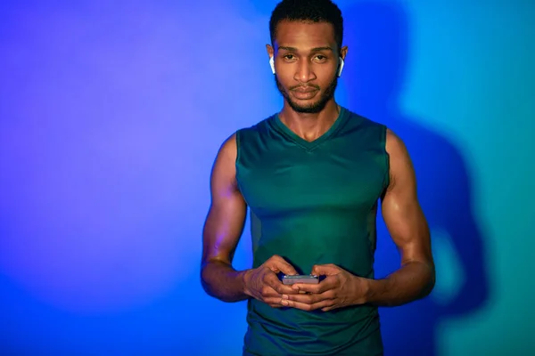 Fitness-Typ mit Handy, Ohrhörer, blauer Hintergrund, Studio — Stockfoto