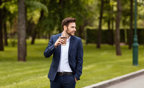 Millennial affärsman njuter av sin hämtkaffe när du går i parken under pausen — Stockfoto