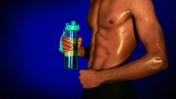 Black Fitness Guy håller flaska på blå studio bakgrund, beskuren — Stockfoto
