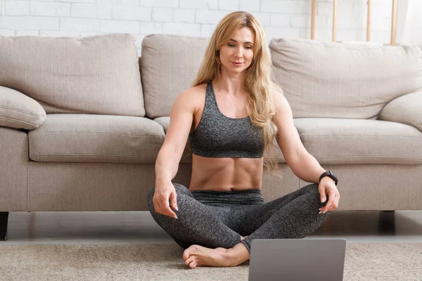 Watch video or record blog. Woman sitting on floor in lotus position looks at laptop