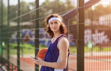 Çekici Kafkasyalı sporcu açık hava sahasında cep telefonuyla internete göz atıyor.