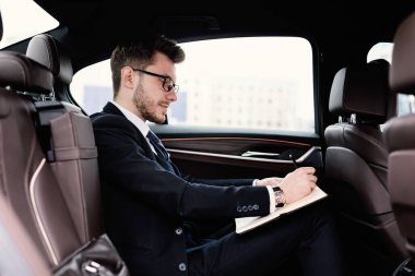 İşadamı, lüks arabasıyla deftere bir şeyler yazıyor.