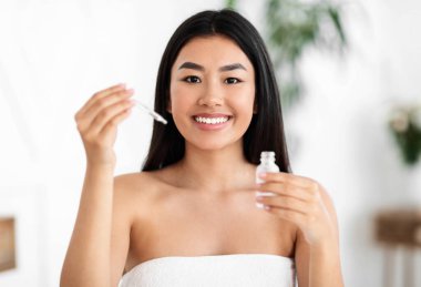 Mutlu Asyalı kız yeni yüz serumunu evde test ediyor.