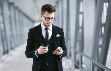 Odaklanmış iş adamı cep telefonuna mesaj atıyor, kahve içiyor.