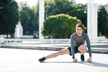 Eğitimden önce kasları ısıtmak için egzersiz. Spor giyimli bir adam parkta egzersiz yapıyor.