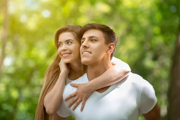 Atraente millennial cara carregando namorada em suas costas no parque verde — Fotografia de Stock