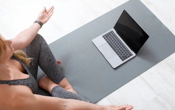 Workout zu Hause online. Frau meditiert in Lotus-Pose auf dem Boden auf Sportmatte mit Laptop — Stockfoto