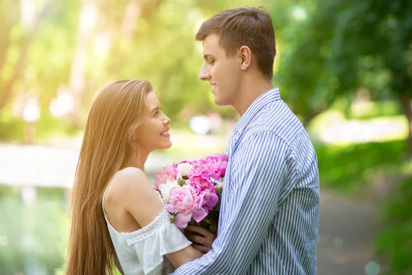 Świętujemy rocznicę. Kochająca para z bukietem piwonii kwiaty w parku w letni dzień — Zdjęcie stockowe