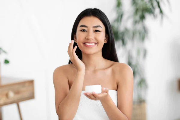 Alegre ásia mulher aplicação creme no ela rosto — Fotografia de Stock