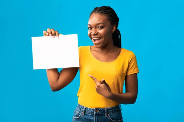 Mujer africana mostrando póster de papel en blanco sobre fondo azul del estudio — Foto de Stock