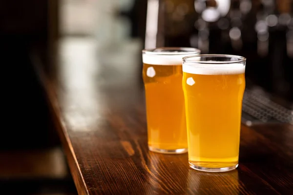 Deliciosas bebidas frías. Dos vasos de cerveza ligera en el mostrador de bar de madera en el pub — Foto de Stock