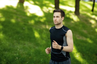 Yaz sporu. Spor kıyafetli, spor takip cihazlı bir adam parkta koşuyor.
