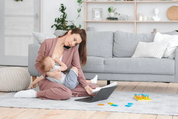 Young Mom Working On Laptop And Talking On Cellpone While Breastfeeding Baby