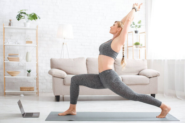 Fitness at home online. Woman in sportswear on sports mat with laptop in living room