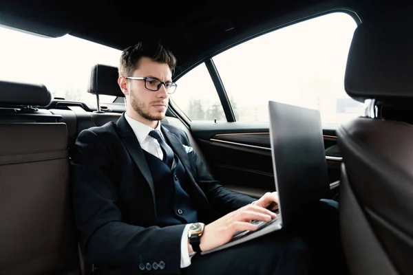 Empresário sério ocupado usando seu laptop em carro de luxo — Fotografia de Stock