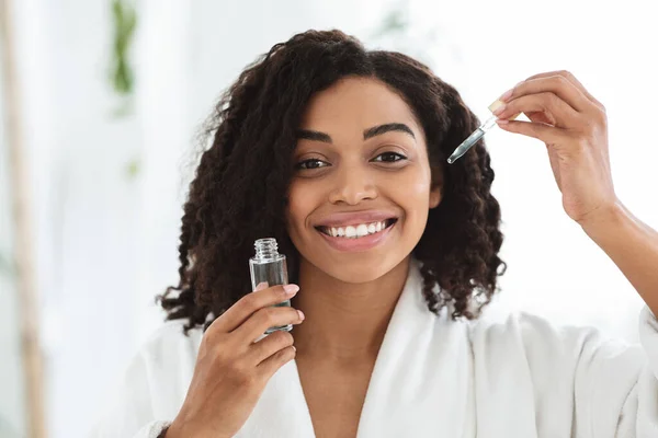 Produits de soins de la peau. Sourire femme africaine tenant bouteille avec sérum hydratant visage — Photo