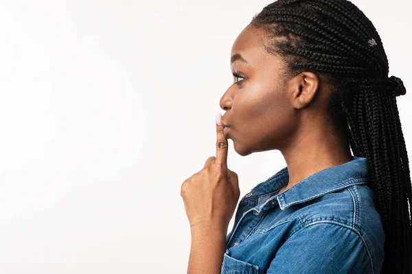 Femme noire gesticulant doigt sur les lèvres signe, fond blanc, vue de côté — Photo