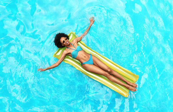 Афроамериканка в купальнике, плавающая в надувном матрасе у бассейна, вид сверху
