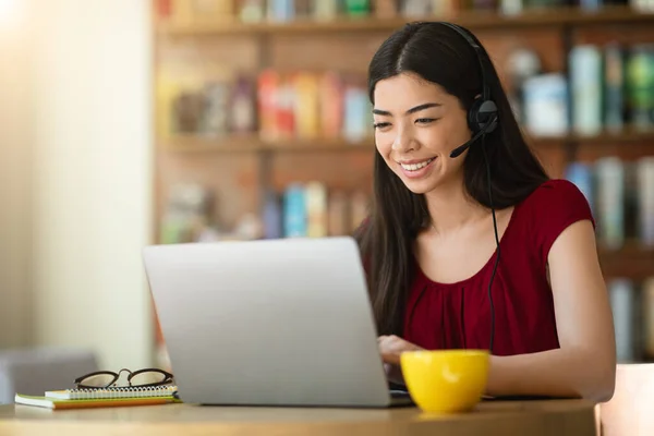 Tutoría en línea. Asiática mujer tutora con auriculares trabajando en portátil en café —  Fotos de Stock