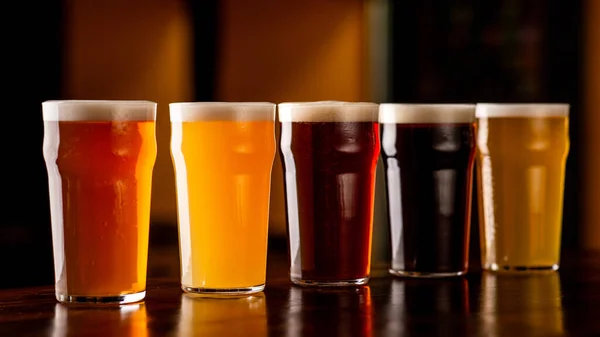 Pivní mix v hospodě. Tma, světlo, ječmen, ležák a pivo v brýlích na hnědém dřevěném pultu — Stock fotografie