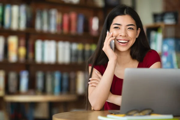 Hübsch asiatisch mädchen talking auf handy während sitting mit laptop im cafe — Stockfoto