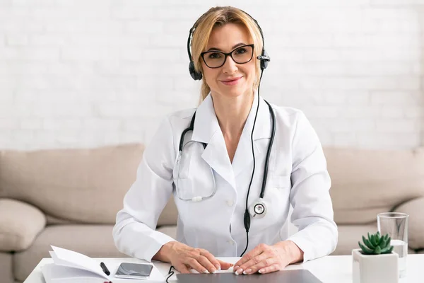 Online ιατρική γνωμάτευση, διαμονή στο σπίτι. Γιατρός κάθεται στο χώρο εργασίας με φορητό υπολογιστή — Φωτογραφία Αρχείου