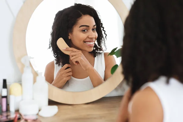 Attractive African Woman Combing Her Hair In Front Of Mirror At Home — Stock Photo, Image