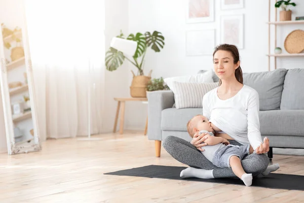 Relaxado jovem mãe meditando enquanto amamenta seu bebê em casa, praticando Yoga — Fotografia de Stock