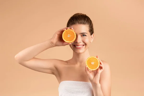 Naturalny detoks skóry. Promienna młoda dziewczyna trzyma plasterki świeżej pomarańczy na beżowym tle — Zdjęcie stockowe