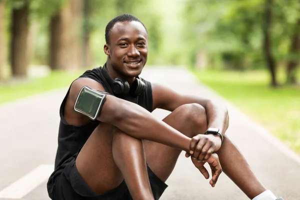 Χαρούμενος μαύρος αθλητής που κάθεται στο μονοπάτι του πάρκου, ξεκουράζεται — Φωτογραφία Αρχείου